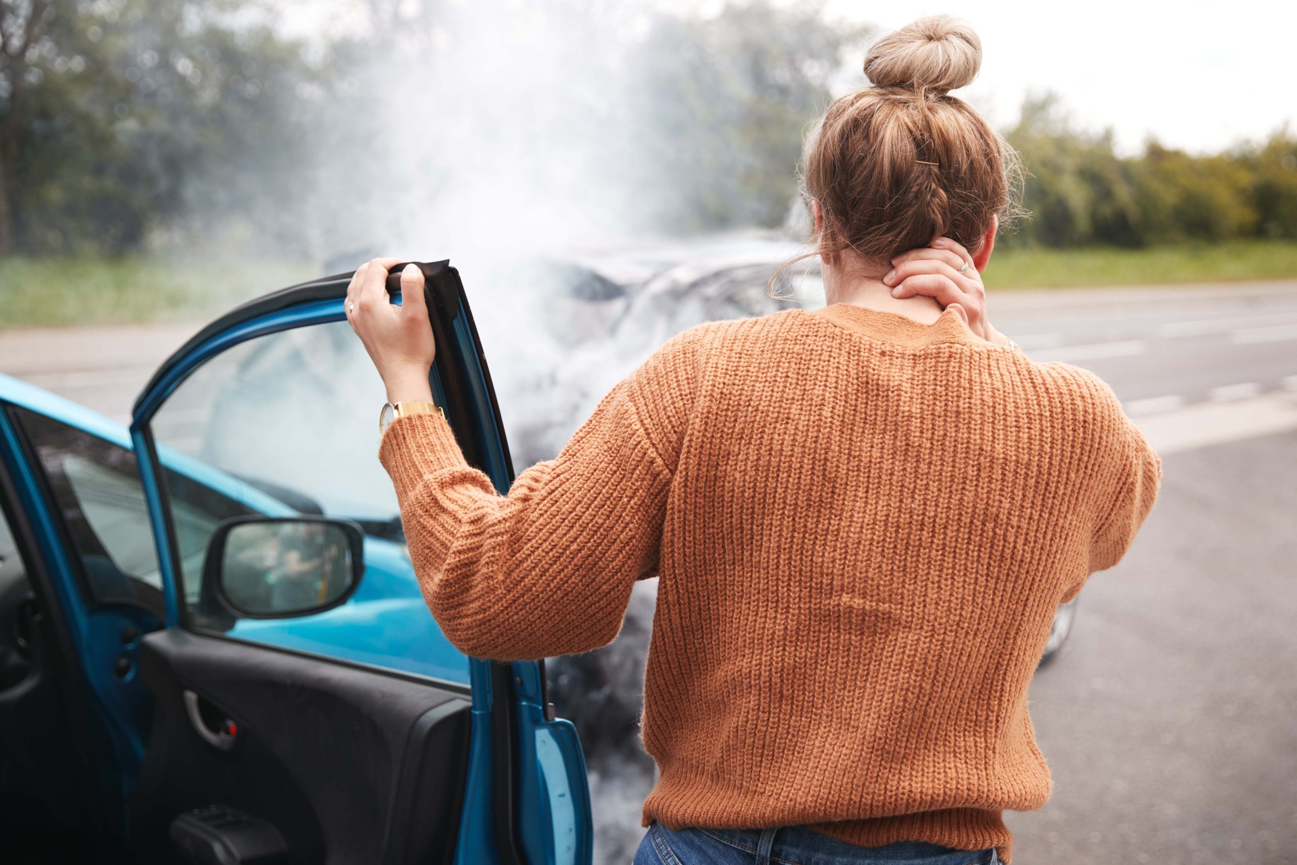 Rear View Of Female Motorist With Head Injury Getting Out Of Car After Crash Auto Accident with Girl holding her neck by her car